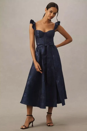 Model wearing a dark blue midi dress with ruffled straps and a matching tie belt against a plain grey backdrop