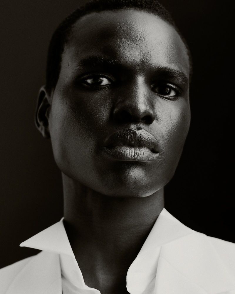 Striking close-up portrait of a Black male model in a white collared shirt against a dark backdrop, showcasing editorial fashion.