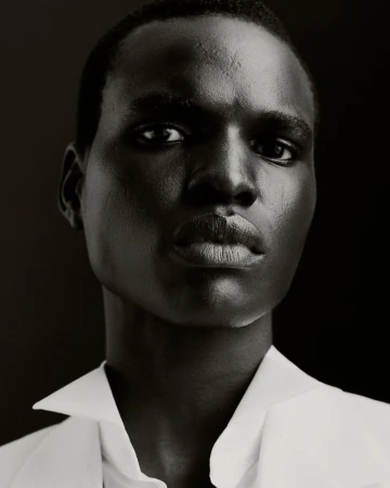 Striking close-up portrait of a Black male model in a white collared shirt against a dark backdrop, showcasing editorial fashion.