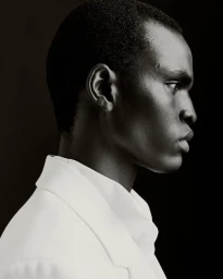Profile portrait of a Black man wearing a white jacket against a dark background, photographed by Álvaro Pereña Jimenez for Zara.