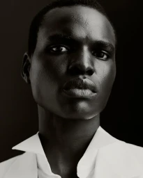 Close-up monochrome portrait of a male model wearing a white collared shirt against a dark background.