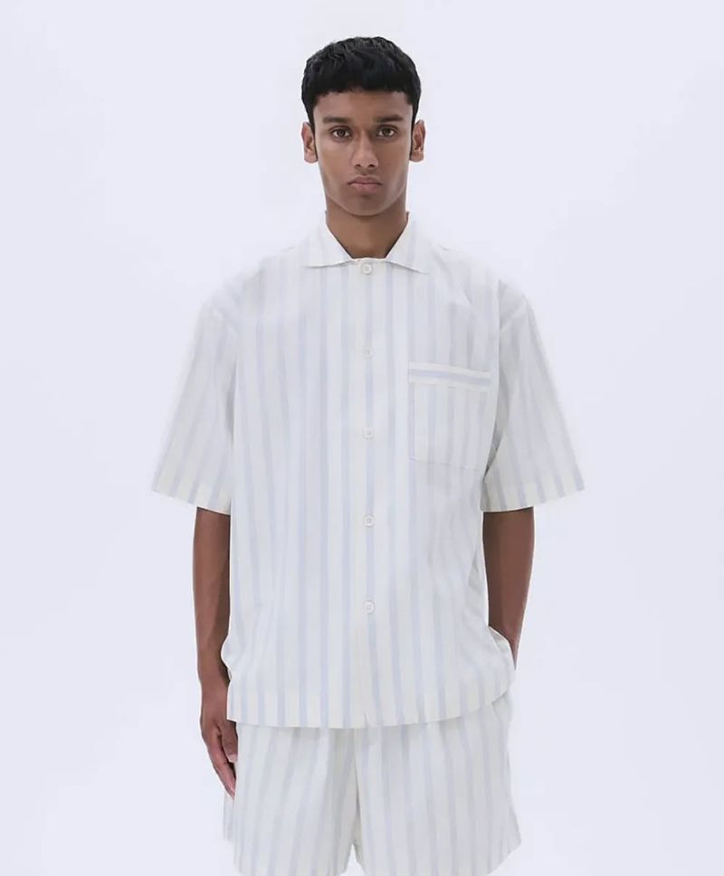 Man in a matching striped shirt and shorts set stands in a bright white studio with soft lighting, looking directly at the camera.