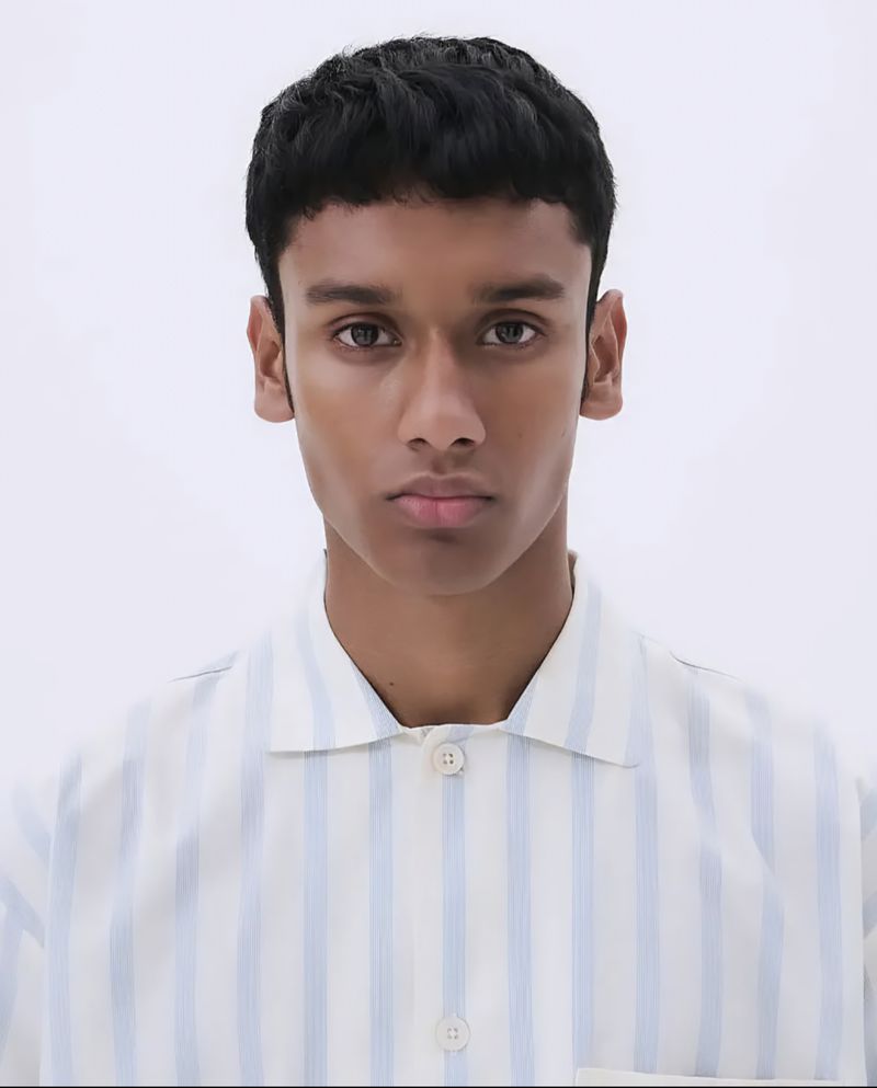 Close-up studio shot of a young adult male with short dark hair wearing a blue and white striped shirt against a white backdrop.