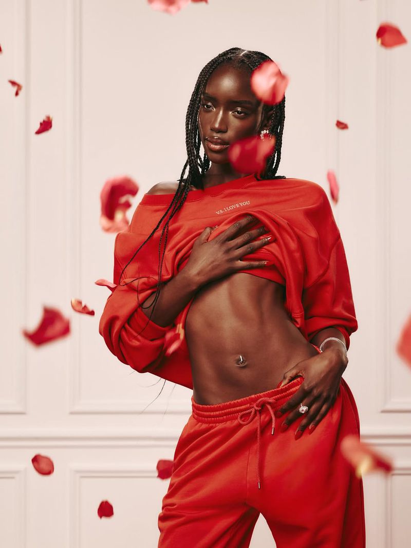 Portrait of a black woman in a red off-the-shoulder sweatshirt and sweatpants surrounded by red rose petals in a studio setting.