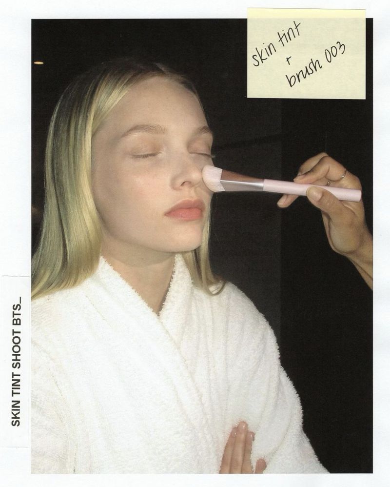 Close-up of a fair-skinned model getting makeup applied with a brush in a studio setting, creating a beauty or fashion shot.