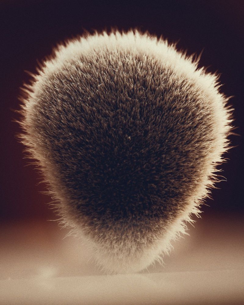Close-up studio shot of a makeup brush with soft, gray bristles against a blurred background, emphasizing texture and detail in muted tones.