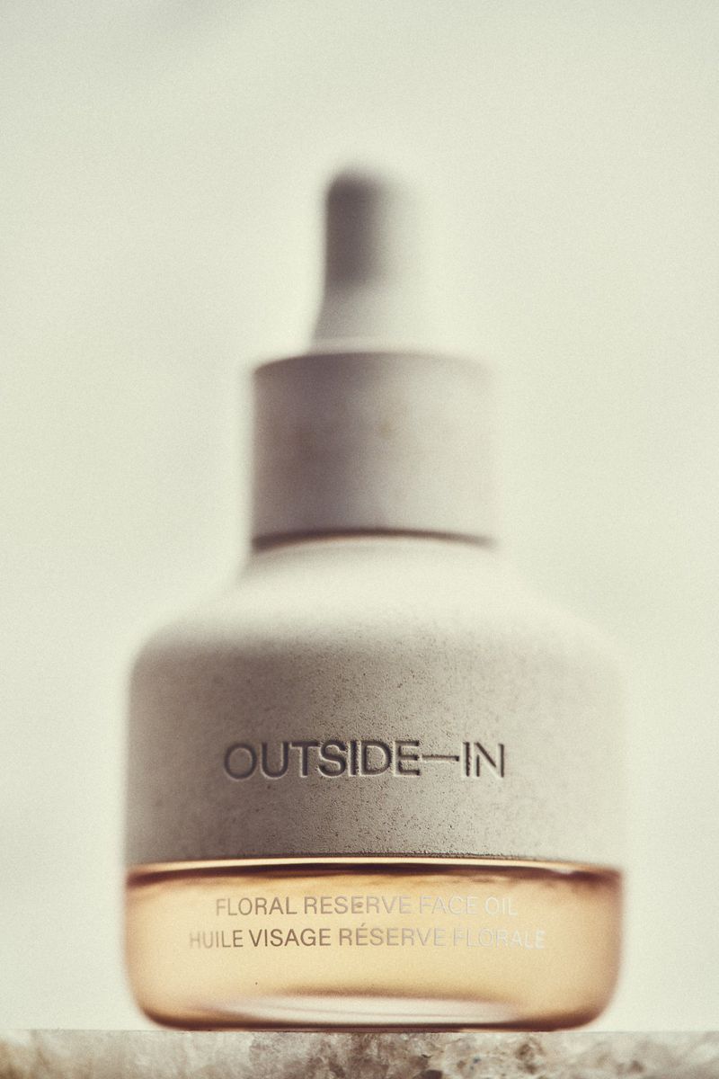 Close-up of a bottle of face oil with a dropper. The bottle has a stone-like texture and is labelled 'OUTSIDE-IN' and 'FLORAL RESERVE FACE OIL'.