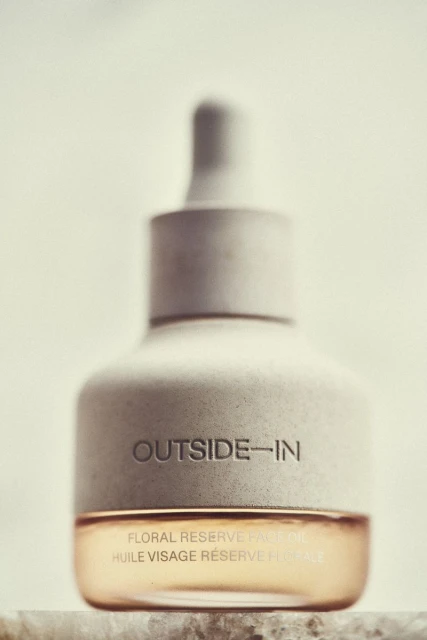 Close-up of a bottle of face oil with a dropper. The bottle has a stone-like texture and is labelled 'OUTSIDE-IN' and 'FLORAL RESERVE FACE OIL'.