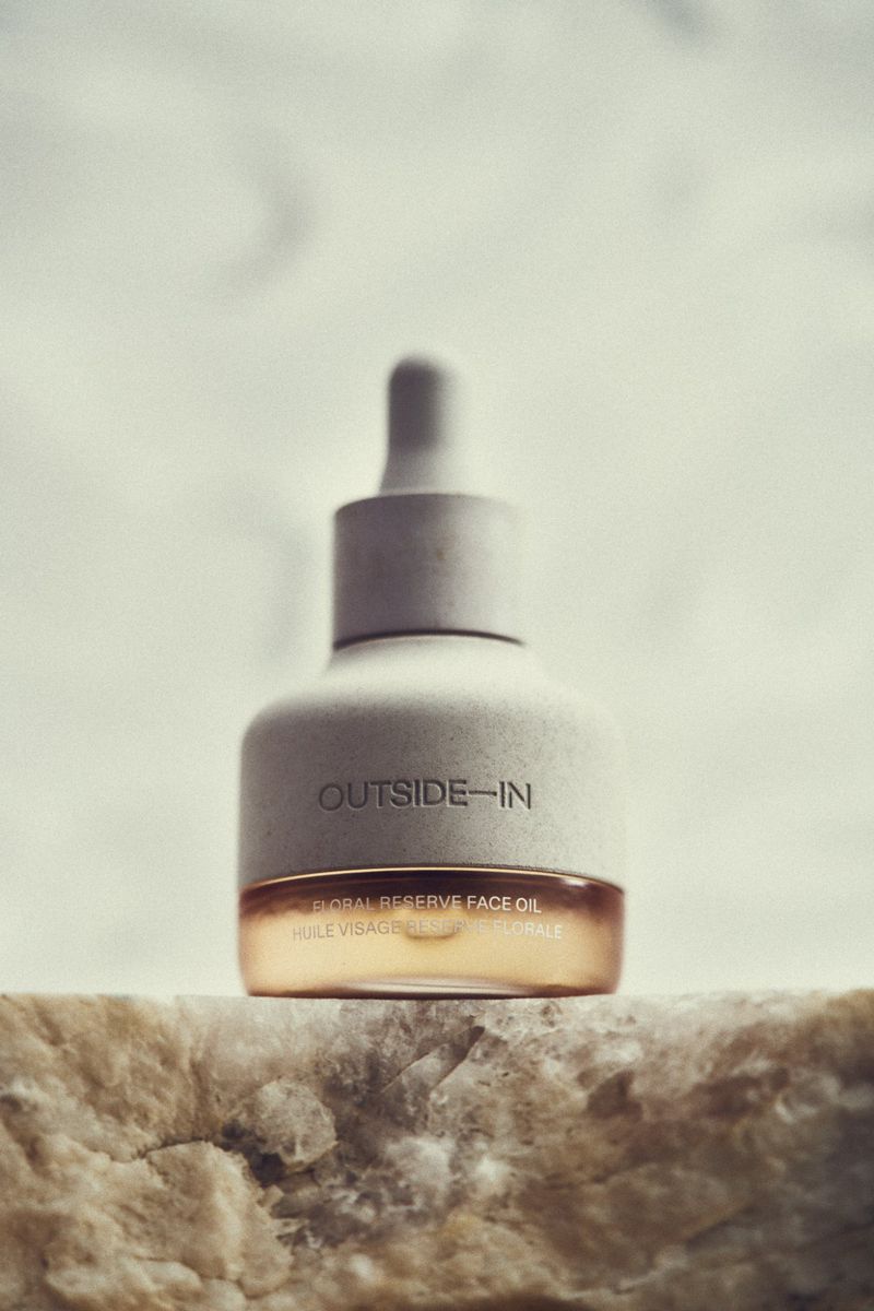 Close-up of a bottle of Outside-In Global Reserve face oil with dropper, resting on a rock surface against a neutral background.