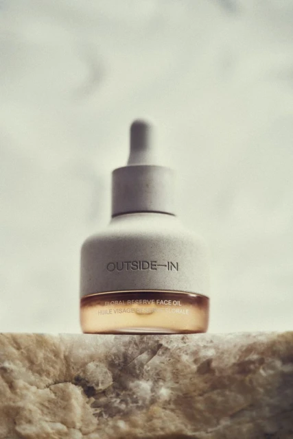 Close-up of a bottle of Outside-In Global Reserve face oil with dropper, resting on a rock surface against a neutral background.