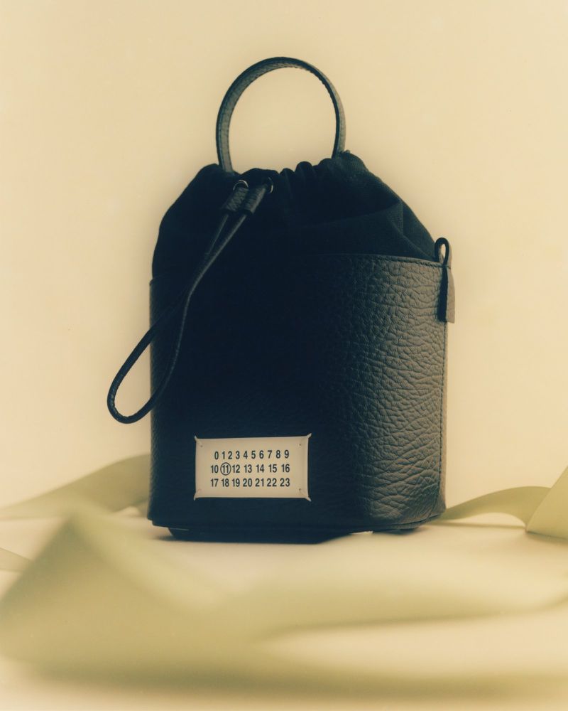 Black Maison Margiela bucket bag with leather bottom and fabric top on a white surface, featuring a logo tag and ribbon detail.