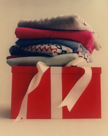 Stacked colorful sweaters on a red gift box with white ribbon, creating a cozy and festive scene with a soft, inviting ambiance.