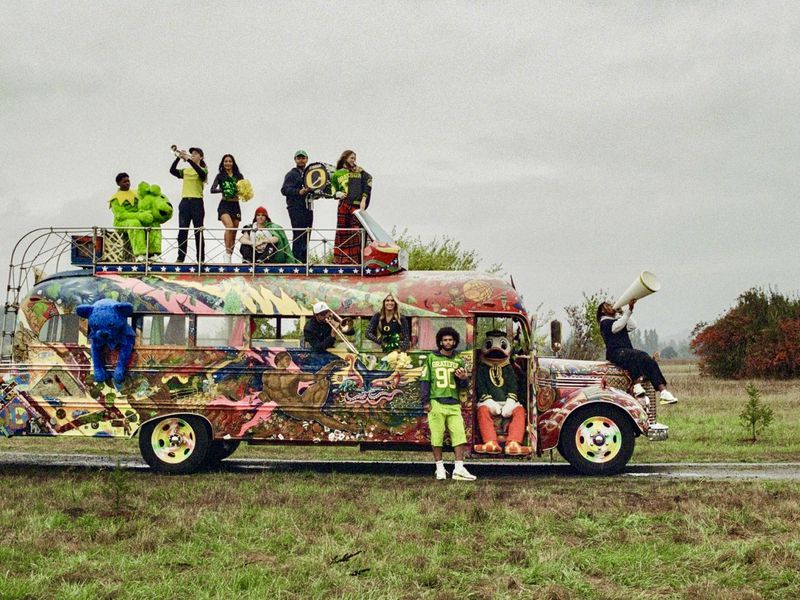 Painted bus with people on top, vintage automobile, mascot, musical instruments. Cheerful, energetic group scene outdoors in daytime.
