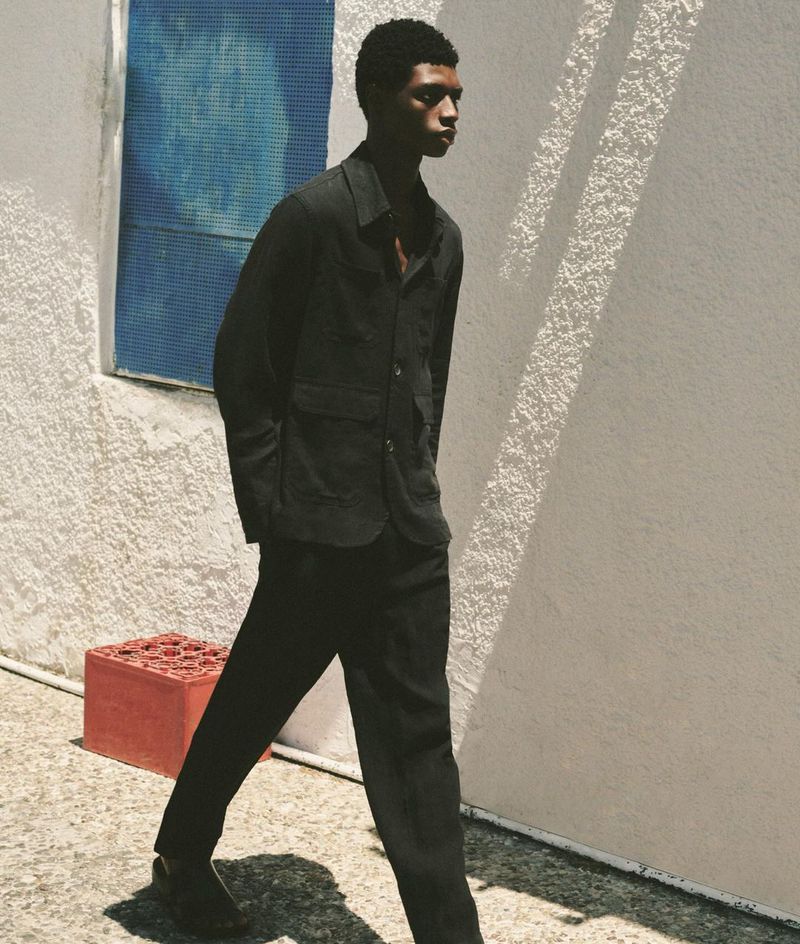 Fashionable Black man walks outdoors in a dark jacket and trousers, sunlight and shadows add depth and interest to the composition.