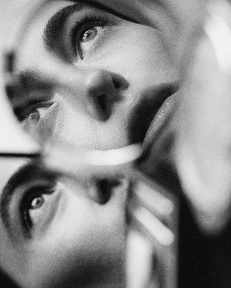 Monochrome close-up portrait of a face reflected and refracted through curved glass with soft light and film grain.