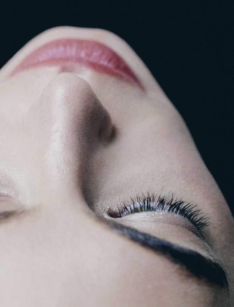 Extreme close-up macro portrait of a model face with closed eyes against a dark background, photographed by Paul Scala.