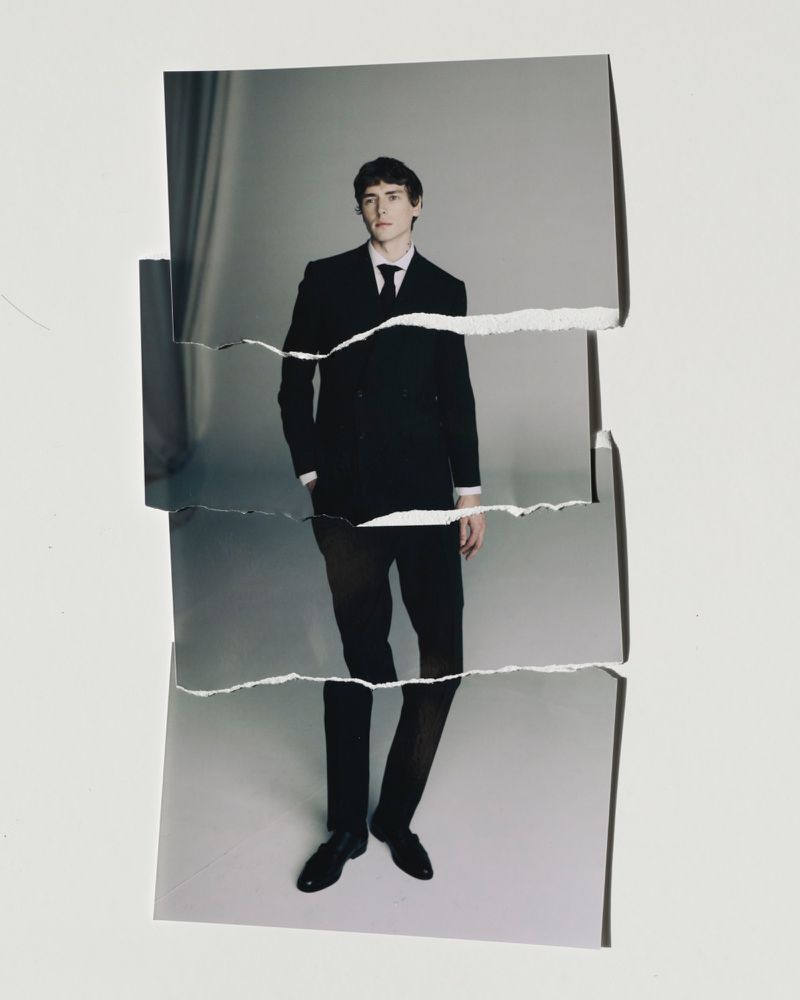 Torn photograph of a man in a black suit standing in front of a gray background. Formal wear, studio lighting, fashion concept.