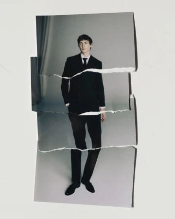 Torn photograph of a man in a black suit standing in front of a gray background. Formal wear, studio lighting, fashion concept.