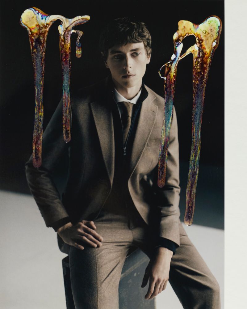 Young man in tailored suit with artistic abstract drizzles. Fashion-forward studio portrait featuring stylish formal wear in a contemporary composition.