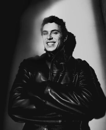 Portrait of actor Ar3n Piper wearing a dark leather jacket with arms crossed against a plain wall.