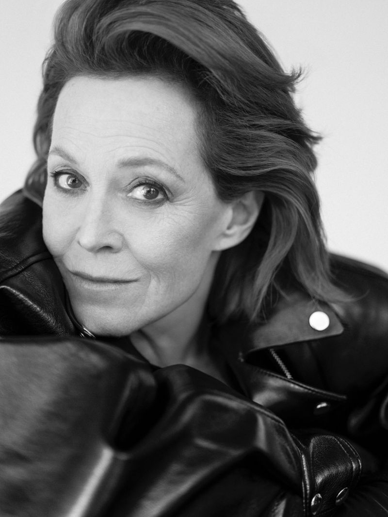 Black and white portrait of older woman with short wavy hair wearing a black leather jacket against a neutral background.