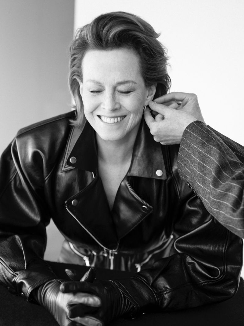 Black and white portrait of a smiling middle-aged woman with short hair, wearing a leather jacket, as someone adjusts her earring.
