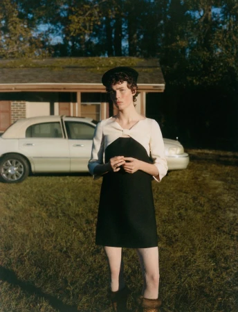 Model wearing a black and white dress and beret posing outdoors in front of a house and car for Vogue Polska