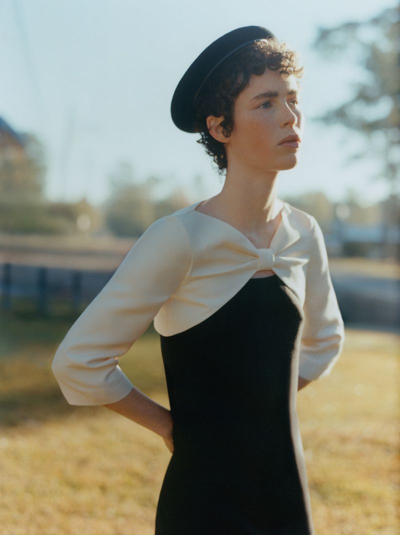 Model Jesi Evans wearing a black beret and an ivory bow-front shrug over a black dress against a soft outdoor background.
