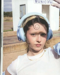 Close-up portrait of a woman wearing light blue over-ear headphones and a white t-shirt with a gelled spiral curl on her forehead.