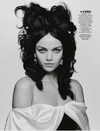 Model with voluminous dark historic hairstyle and pearl hairpins wearing an off-shoulder white top against a grey backdrop