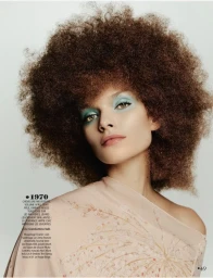 Model Marie-Louise Wedel with voluminous curly hair and light blue eyeshadow in a peach top against a pale studio background.