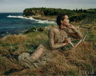 Woman in an intricate lace dress lying in coastal grass next to a folding chair overlooking the ocean and rocky cliffs