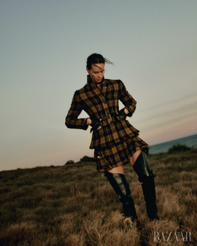 Woman wearing a plaid coat and tall boots standing in a field at dusk