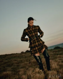 Woman wearing a plaid coat and tall boots standing in a field at dusk