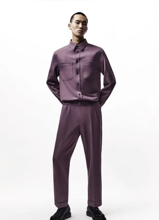 A stylish male model poses in a light purple, long-sleeved button-down shirt and matching trousers against a stark white background.