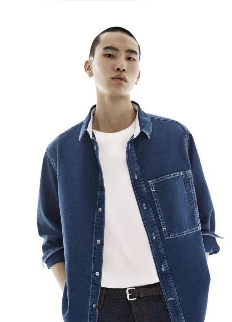 An Asian male model poses in a medium shot, wearing a blue denim shirt and a white tee, against a clean white background.