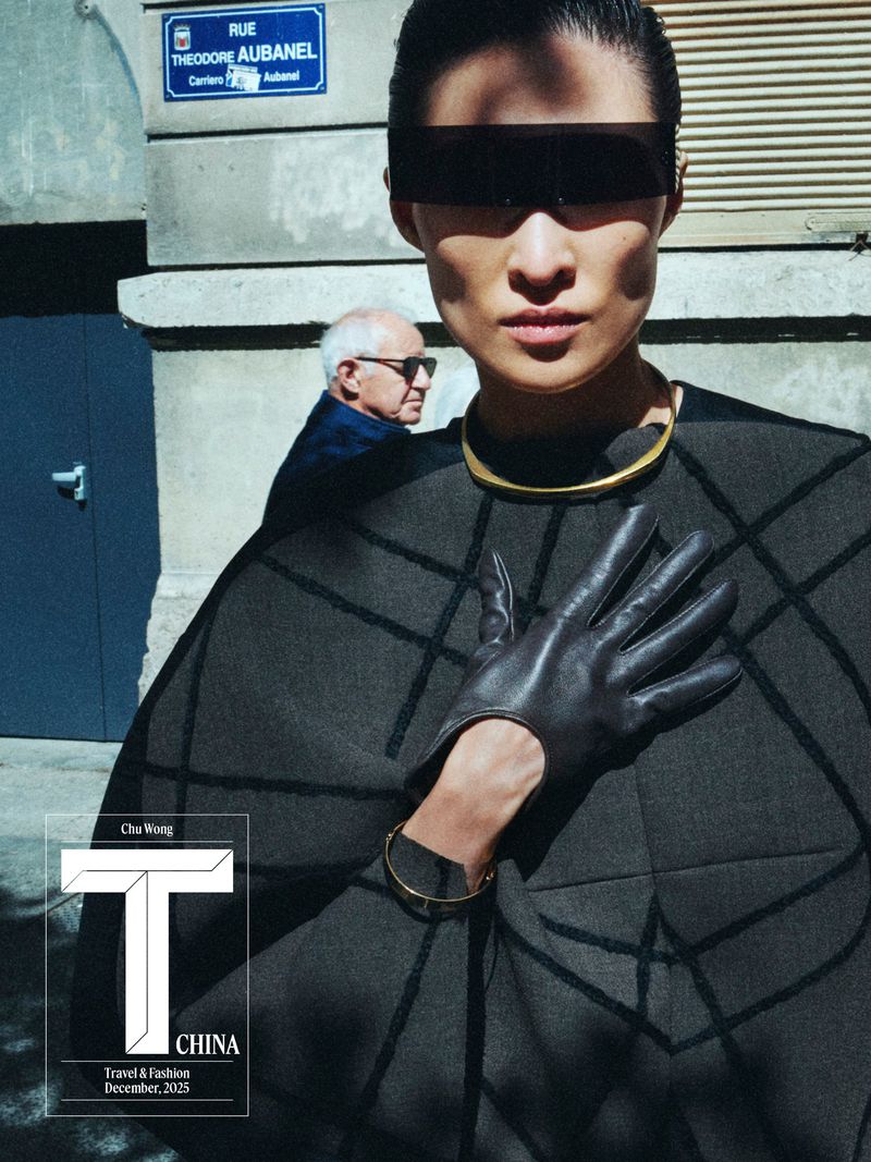 Fashion editorial shot outdoors featuring an Asian model in a modern cape with sunglasses and gloves, complemented by an elderly man in the background.