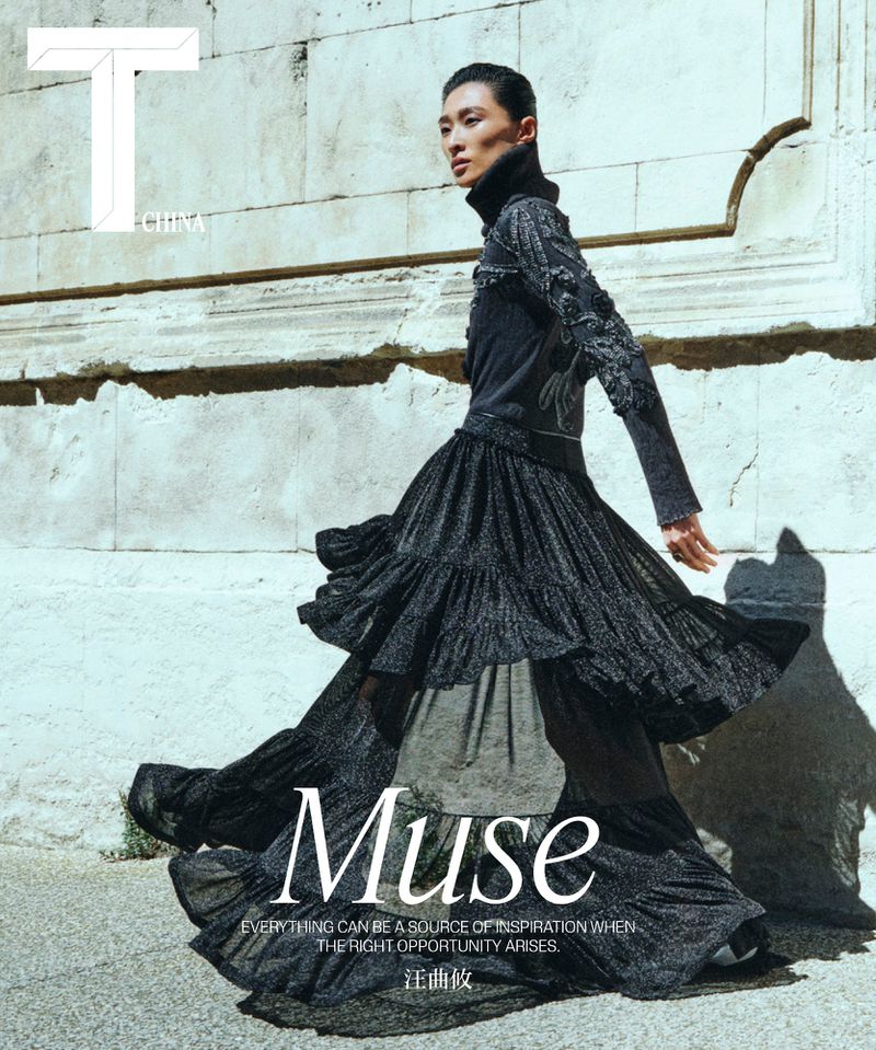Asian fashion model poses outdoors in a black tiered, ruffled dress with a high neck against a stone wall for a fashion magazine cover.