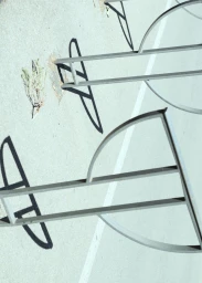 Metal bicycle racks casting crisp geometric shadows on paved ground in bright sunlight.