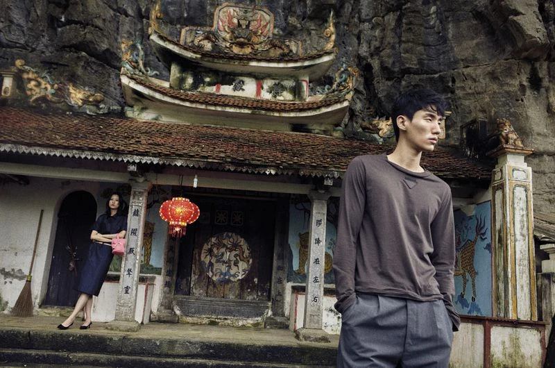Asian male model poses in front of an old Asian temple structure with a woman in a navy dress and a red Chinese lantern.