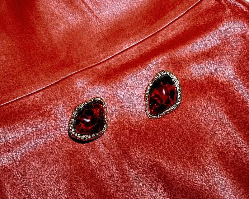 Close-up of two red stone earrings with gold settings on a red leather surface, jewelry product shot.