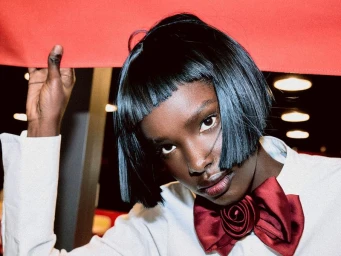 Model Abuk Mayen with a black blunt bob and red satin rose bow tie holding a red banner overhead.