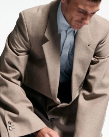 Mature adult man wearing a suit and blue shirt looking down, shot against a white background in a studio setting.