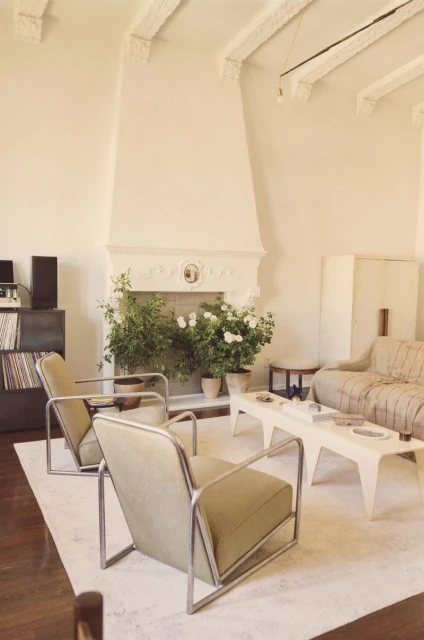 Living room interior with modern armchairs, fireplace with floral decor, geometric coffee table, and decorative wall and ceiling details.