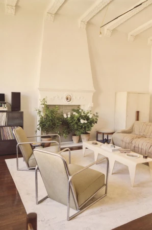 Living room interior with modern armchairs, fireplace with floral decor, geometric coffee table, and decorative wall and ceiling details.