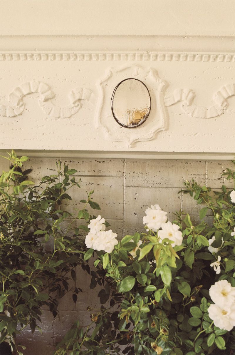 White roses and green foliage surround an antique mirror on a mantelpiece, creating a serene indoor still life scene.