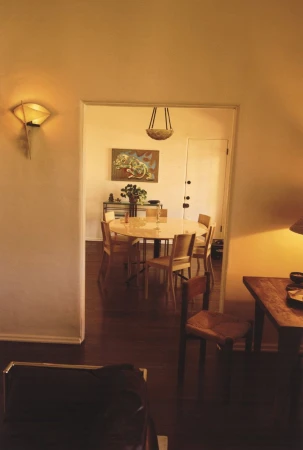 Interior shot of a dining room table and chairs visible through a doorway, featuring a wall-mounted light and dark hardwood floors.