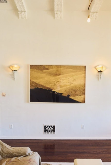 Framed sepia-toned landscape art on a white wall between sconces, above dark wood trim in an interior room setting.