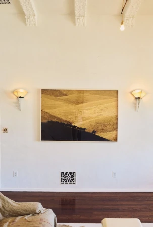 Framed sepia-toned landscape art on a white wall between sconces, above dark wood trim in an interior room setting.