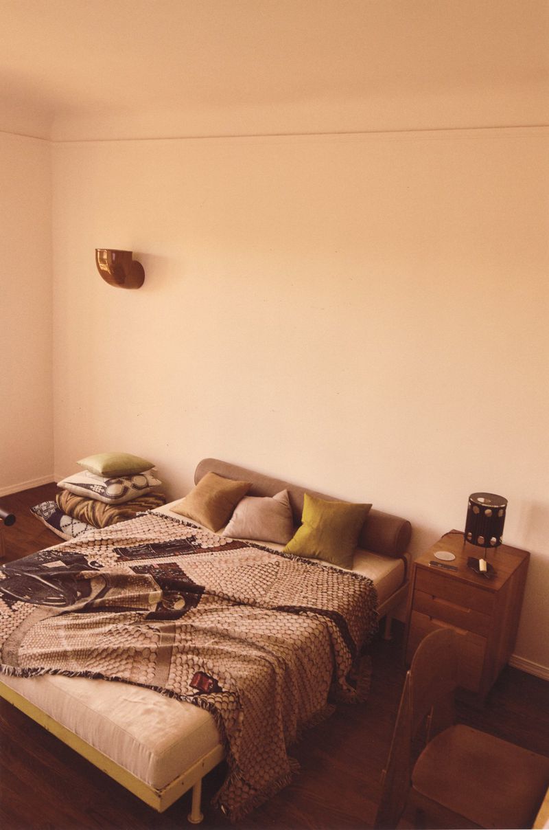 Bedroom interior featuring a made bed with a patterned blanket, pillows, a wooden nightstand, and a brown wooden chair. 